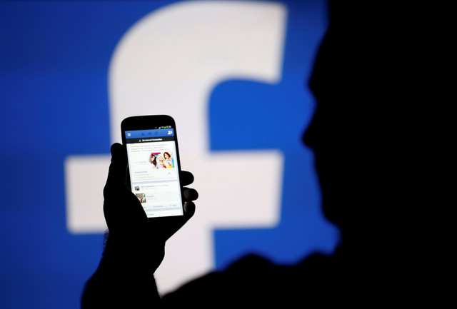 Siluet seorang pria nampak tengah memegang handphone dengan logo Facebook di belakang (Foto: Reuters)