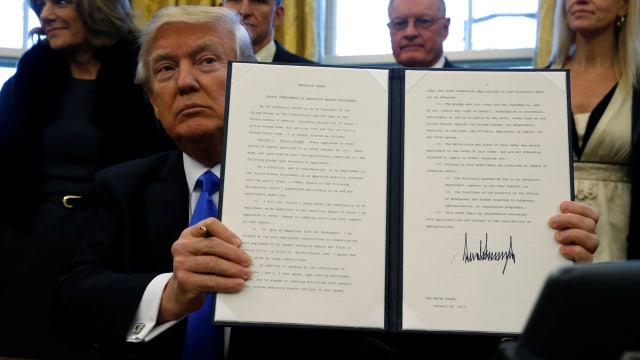 Donald Trump menunjukkan isi executive order. (Foto: Jonathan Ernst/Reuters)