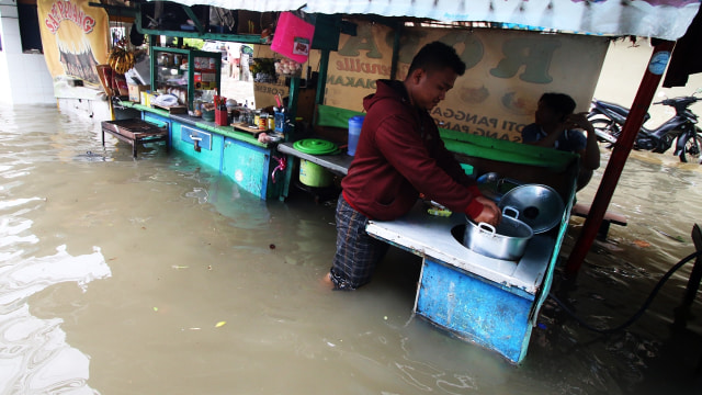 Pedagang memasak di tengah banjir. (Foto: Antara/Rivan Awal Lingga)