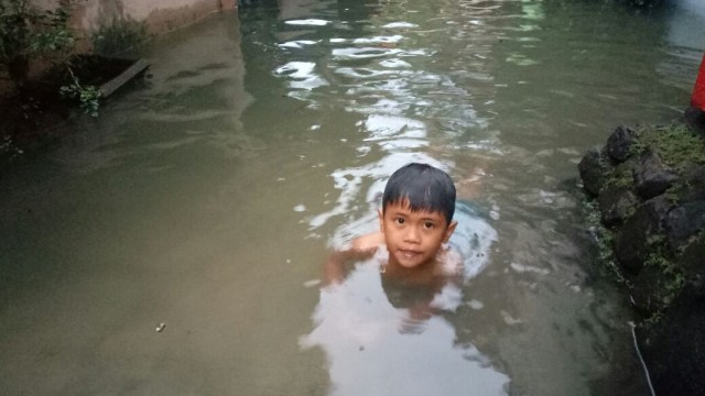 Seorang anak kecil berenang saat banjir di Kemang. (Foto: Musatqim Amna/kumparan)