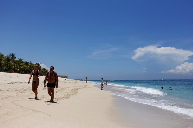 Turis berjalan di pinggir Pantai Bali. (Foto: Reuters/Nyimas Laula)