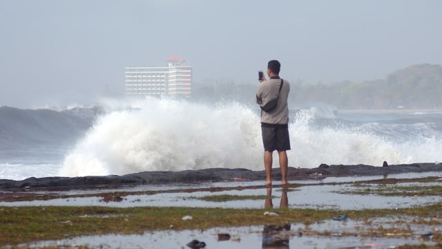 Warga menyaksikan gelombang tinggi di kawasan Pantai Padang Galak, Denpasar, Bali, Rabu (25/7). (Foto: ANTARA FOTO/Wira Suryantala)