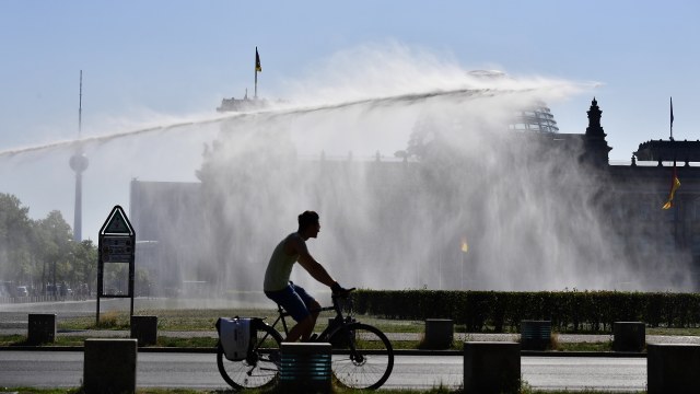 Seorang pria melintas ketika polisi Berlin menggunakan meriam air menyirami taman publik di depan gedung Reichstags, Bundestag, di Berlin Jumat (27/7).
 (Foto:  SCHWARZ / AFP/Tobias Schwarz)