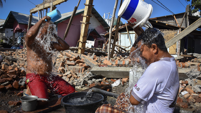 Dua orang korban gempa mandi dekat rumah mereka yang roboh pascagempa di Dusun Lengkukun, Kecamatan Kayangan, Lombok Utara, NTB, Sabtu (11/8/2018).  (Foto: ANTARA FOTO/Ahmad Subaidi)