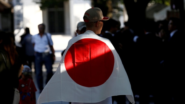 Seorang pria yang mengenakan bendera nasional Jepang mengunjungi Kuil Yasukuni di Tokyo, Jepang, Rabu (15/8/2018). Foto: Reuters/Kim Kyung-Hoon