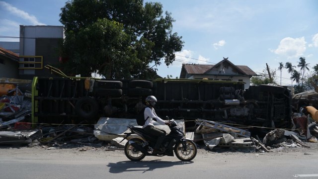 Pengendara melintasi mobil truk yang terbalik di Palu Utara pasca gempa berkekuatan 7,4 Magnitudo dan tsunami. (Foto: Jamal Ramadhan/kumparan)