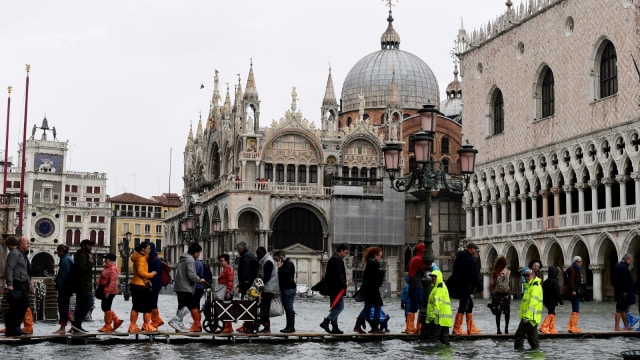 Orang-orang berjalan di atas jembatan gantung di St Mark Square yang terkena banjir di Venesia. (Foto: AFP/Miguel MEDINA)