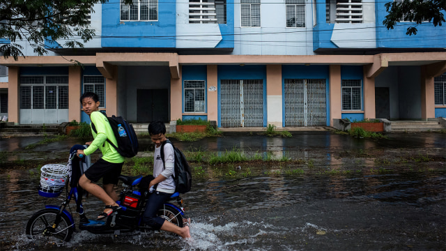 Dua orang anak bersepeda melewati genangan air di perumahan negara yang dibangun untuk penghuni kanal informal di Kota Ho Chi Minh. (Foto: Kao Nguyen / AFP)