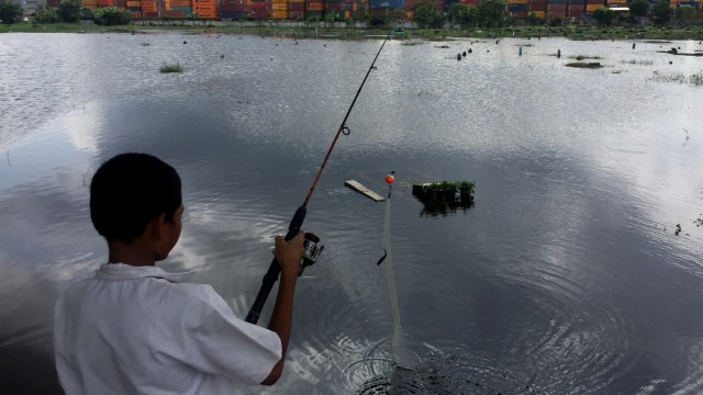 Seorang anak sedang memacing di Tempat Pemakaman Umum (TPU) Semper, Cilincing, Jakarta Utara yang terendam banjir.  (Foto:  Fachrul irwinsyah/kumparan)