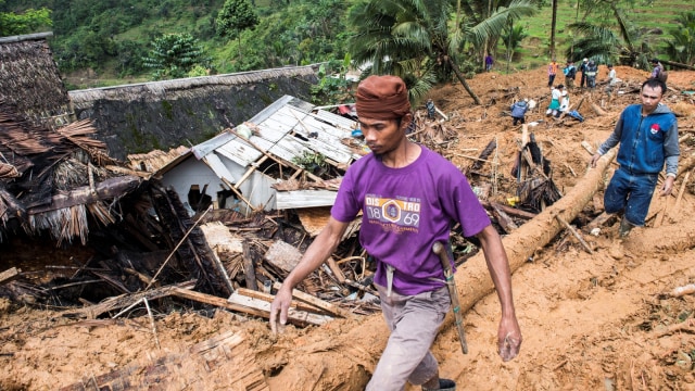 Warga melintas di dekat reruntuhan bangunan akibat tanah longsor di Desa Sirnaresmi, Kecamatan Cisolok, Kabupaten Sukabumi, Jawa Barat, Selasa (1/1/2019). (Foto: Antara/M Agung Rajasa)