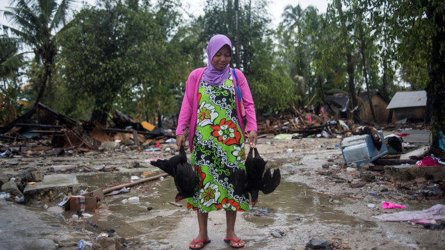 Penyintas tsunami Selat Sunda, Suhana (25) membawa dua ekor ayam dari bekas rumahnya yang rusak diterjang tsunami di Sumur, Pandeglang, Banten, Kamis (3/1).  (Foto: ANTARA FOTO/Sigid Kurniawan)