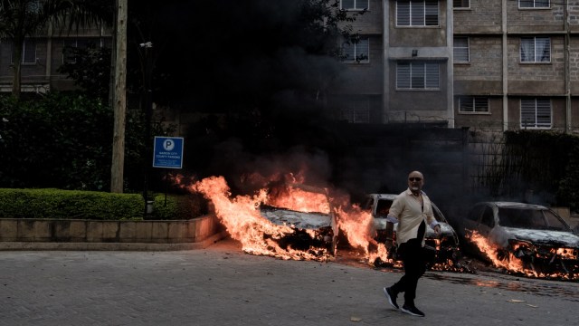 Seorang pria melintas di depan mobil yang terbakar akibat ledakan seragan teroris di Nairobi, Kenya (15/1/19).  (Foto: AFP/KABIR DHANJI)