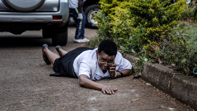 Seorang wanita bersembunyi di belakang  sebuah mobil di tempat ledakan di komplek hotel Westlands Nairobi, (15/1/19).  (Foto: AFP/Luis TATO )