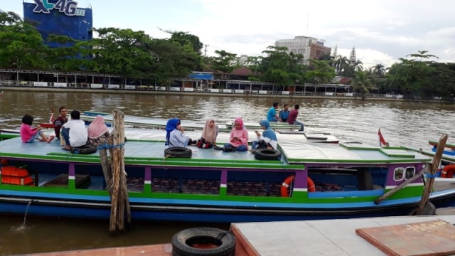 Pelancong menaiki atap klotok ketika susur sungai di Kota Banjarmasin.  Dishub Banjarmasin ingin mengubah kebiasaan ini karena membahayakan wisatawan. Foto: Dok banjarhits.id