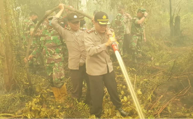 KAPOLRES Bengkalis (depan) saat memegang selang berisi air guna memadamkan api di lahan gambut yang terbakar. 