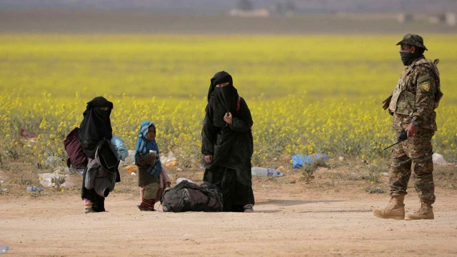 Seorang wanita berdiri dengan barang-barangnya di dekat Baghouz. Foto: REUTERS / Rodi Said