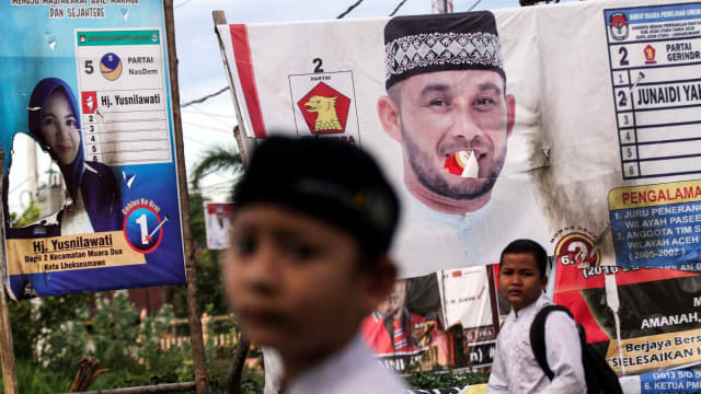 Pelajar melintas di depan Alat Peraga Kampanye (APK) Calon Legislatif (Caleg) yang dibakar orang tak bertanggungjawab di kawasan Muara Dua, Lhokseumawe, Aceh, Sabtu (16/2/2019). Foto: ANTARA FOTO