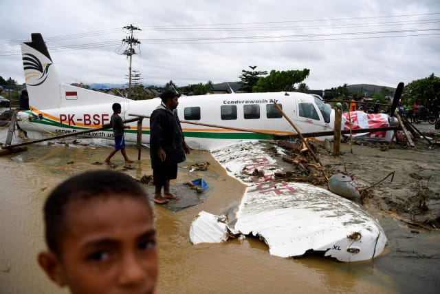 Warga mengamati sebuah pesawat yang terseret banjir bandang di Sentani, Jaya Pura, Papua, Senin (18/3/2019). Akibat banjir bandang yang melanda Sentani sejak Sabtu (16/3) lalu, sedikitnya empat ribu warga mengungsi di sejumlah posko pengungsian. ANTARA FOTO/Zabur Karuru/foc.