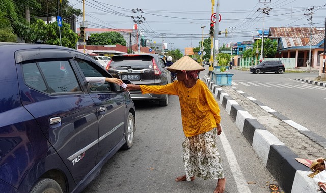 Salah seorang nenek (pengemis) menerima uang dari salah seorang pengendara di Jalan Moh. Hatta, Kota Palu, Minggu (26/5). Foto: PaluPoso