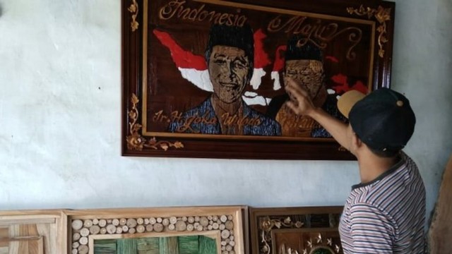 Saiful Huda (35) menunjukkan ukiran limbah kayu sketsa wajah Jokowi-Ma'ruf Amin.