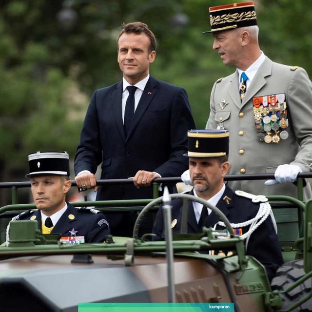 Presiden Prancis Emmanuel Macron (kiri) berdiri di atas kendaraan Acmat VLRA ketika mereka meninjau pasukan sebelum dimulainya militer Hari Bastille menyusuri jalan Champs-Elysees di Paris pada 14 Juli 2019. Foto: AFP