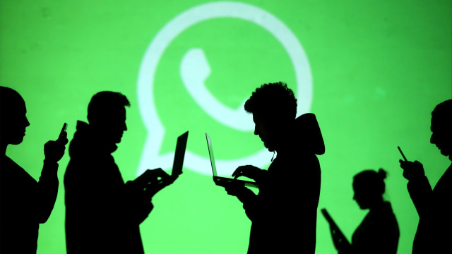 Pengguna laptop dan perangkat seluler terlihat di sebelah proyeksi layar logo Whatsapp. Foto: REUTERS / Dado Ruvic