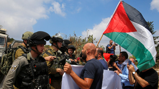 Seorang demonstran memegang bendera Palestina di depan pasukan Israel dalam sebuah protes terhadap permukiman Yahudi dekat Beit Jala di Tepi Barat yang diduduki Israel, Minggu (8/9). Foto: REUTERS/Mussa Qawasma