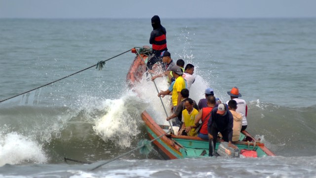 Perahu nelayan menghadang gelombang tinggi saat akan pergi ke laut menggunakan kapal kecil. Foto: ANTARA FOTO/Iggoy el Fitra