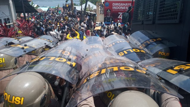 Para polisi terlihat berlindung menggunakan tameng saat massa aksi melempar batu ke arah mobil water canon di depan Kantor DPRD Kota Ternate. Foto: Rizal Syam/cermat