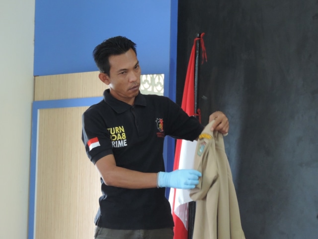 Anggota kepolisian yang menunjukkan baju dinas tersangka yang sobek pada badge dan kancing terlepas. Foto: Dina Mariana/Hi!Pontianak