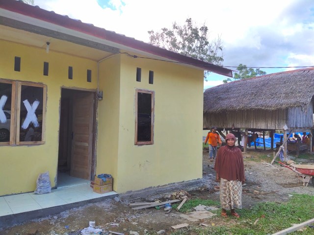 Rahimah, seorang penerima bantuan rumah layak huni dari Pemerintah Aceh berdiri di depan rumahnya yang tengah dibangun. Foto: Humas Setda Aceh