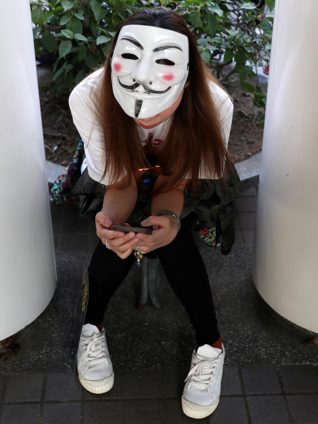 Seorang demonstran anti pemerintah mengenakan topeng Guy Fawkes sambil memeriksa teleponnya pada saat aksi "Menolak Lupa" di Hong Kong, China, Minggu (1/12). Foto: REUTERS/Leah Millis
