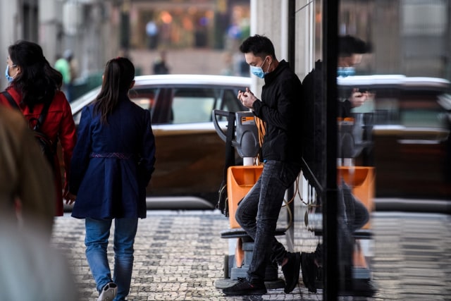 Warga mengenakan masker saat ia berdiri di luar hotel New Orient Landmark di Makau, China. Foto: AFP/Anthony WALLACE
