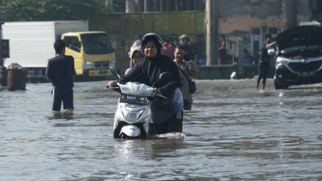 Seorang pengendara roda dua terpaksa mematikan mesin dan mendorong sepeda motornya di jalan yang masih tergenang banjir, Minggu (26/1). (Foto: Ananda Gabriel)