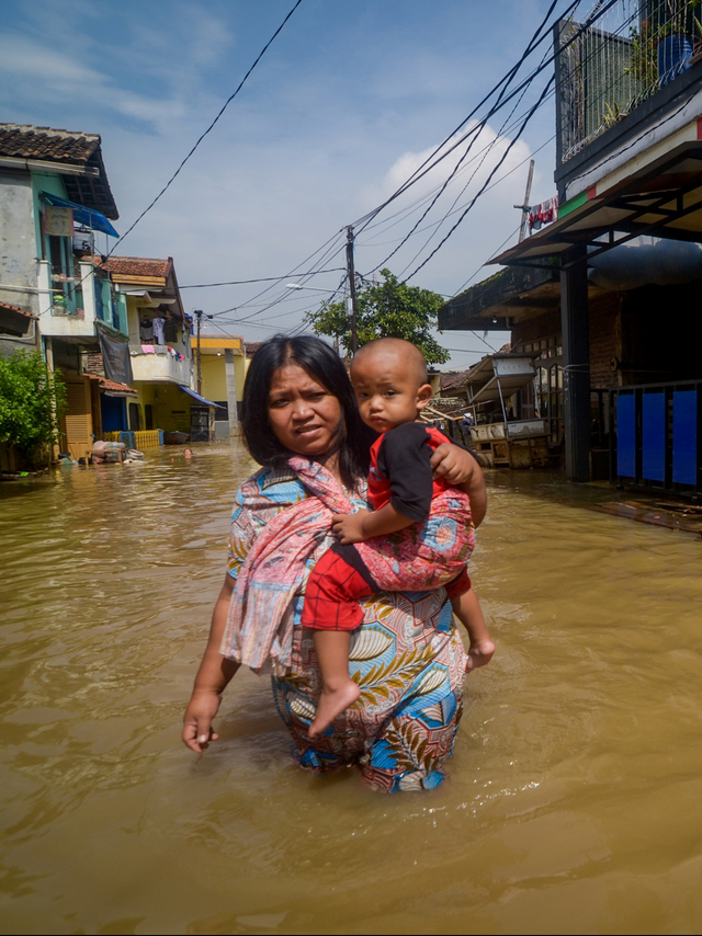 Seorang warga sambil menggendong balita menerjang banjir di Bojongasih, Dayeuhkolot, Kabupaten Bandung, Jawa Barat, Senin (17/2).  Foto: ANTARA FOTO/Raisan Al Farisi