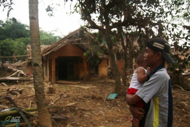 Jahaedi sambil menggendong anaknya berada di depan bekas rumahnya yang hancur akibat banjir bandang di Kampung Seupang, Pajagan, Sajira, Lebak, Sabtu (15/2). (ACTNews/Eko Ramdani)