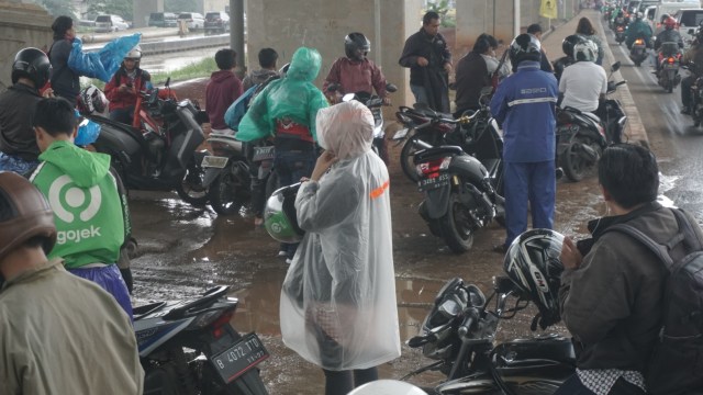 Sejumlah pengendara motor memakai jas hujan saat berteduh di bawah kolong flyover Tol Becakayu, Bekasi, Jumat (21/2).  Foto: Iqbal Firdaus/kumparan 
