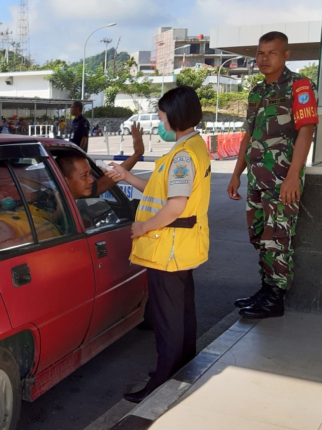 Seorang petugas Kantor Kesehatan Pelabuhan (KKP) Entikong mengukur suhu tubuh pelintas batas yang masuk dari Malaysia di Pos Lintas Batas Negara Entikong. Foto: ANTARA FOTO/Agus Alfian