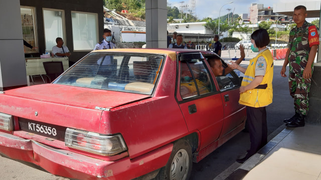 Seorang petugas Kantor Kesehatan Pelabuhan (KKP) Entikong mengukur suhu tubuh pelintas batas yang masuk dari Malaysia di Pos Lintas Batas Negara Entikong. Foto: ANTARA FOTO/Agus Alfian