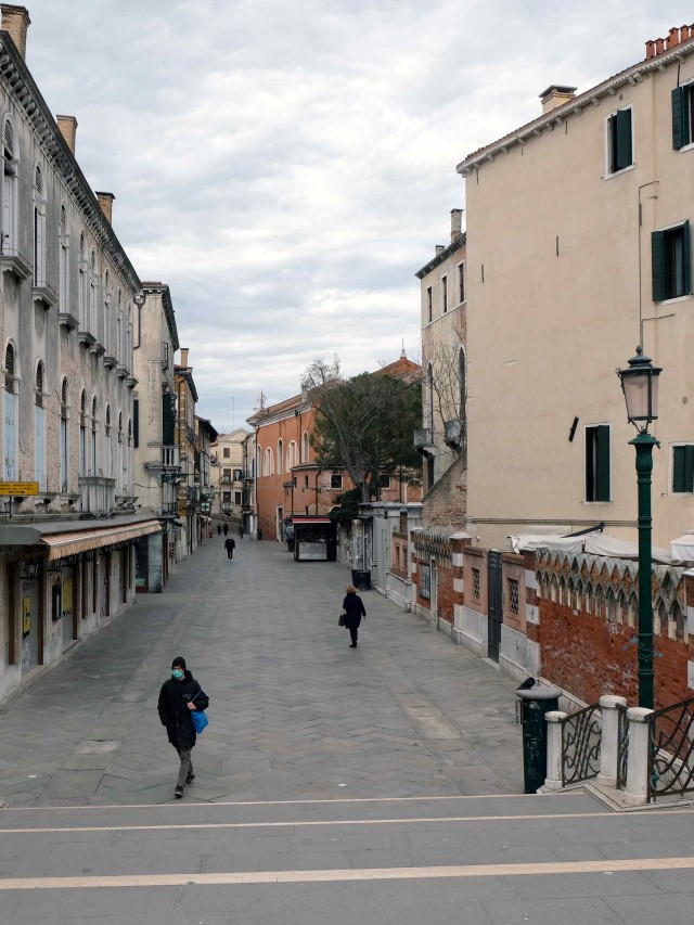 Warga Italia berjalan sambil menggunakan masker di tengah ancaman virus corona. Foto: REUTERS/Manuel Silvestri