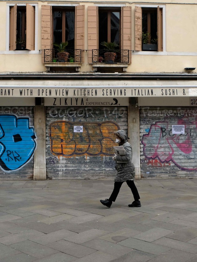 Warga Italia berjalan sambil menggunakan masker di tengah ancaman virus corona. Foto: REUTERS/Manuel Silvestri