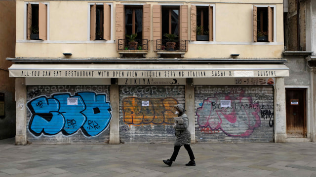 Warga Italia berjalan sambil menggunakan masker di tengah ancaman virus corona. Foto: REUTERS/Manuel Silvestri