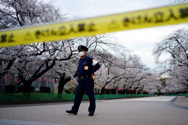 Seorang petugas berjaga di sekitar jalan saat bunga sakura mekar di Taman Ueno, Tokyo, Jepang. Foto: AP / Eugene Hoshiko