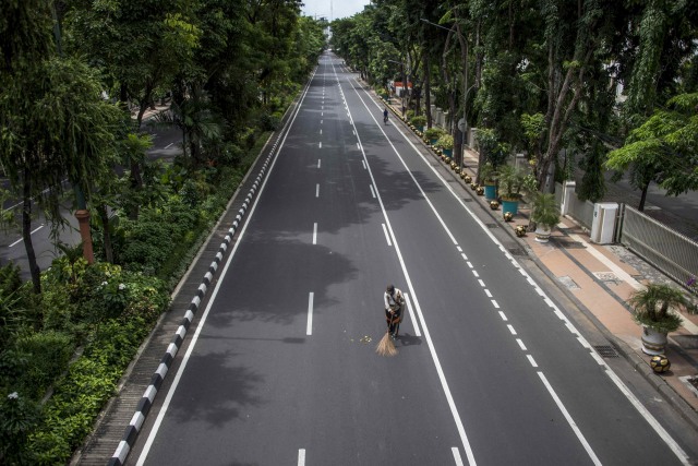 Seorang petugas membersihkan jalan yang ditutup saat physical distancing di Surabaya, Jawa Timur. Foto: AFP/JUNI KRISWANTO