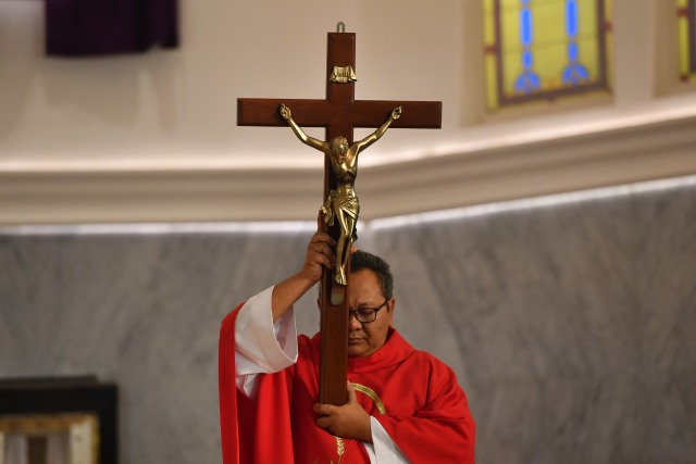 Seorang romo mengangkat salib saat Ibadah Jumat Agung di Gereja Katedral Surabaya, Jawa Timur, Jumat (10/4/2020). Foto: ANTARA FOTO/Zabur Karuru