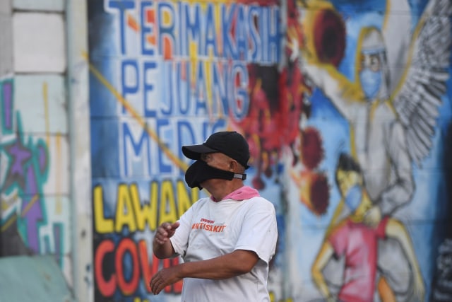 Seorang warga berolah raga dengan latar belakang mural ajakan melawan COVID-19 di Depok, Jawa Barat, Selasa (14/4). Foto: ANTARA FOTO/Wahyu Putro A
