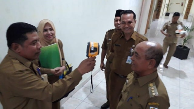 BUPATI Pelalawan, HM Harris, diperiksa suhu tubuhnya oleh petugas saat masuk ke ruang kerjanya. 