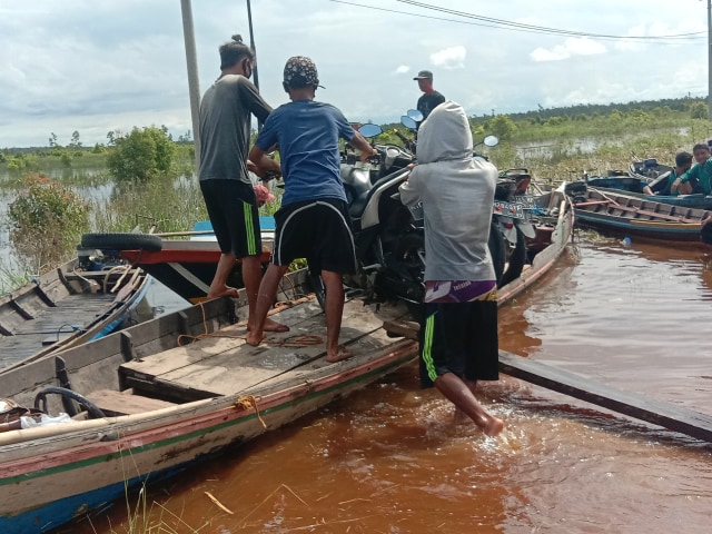 Para penyedia jasa angkutan air saat menaikan kendaraan roda dua untuk menyebrangi banjir di Bukit Rawi, Kalteng, Kamis(7/5).