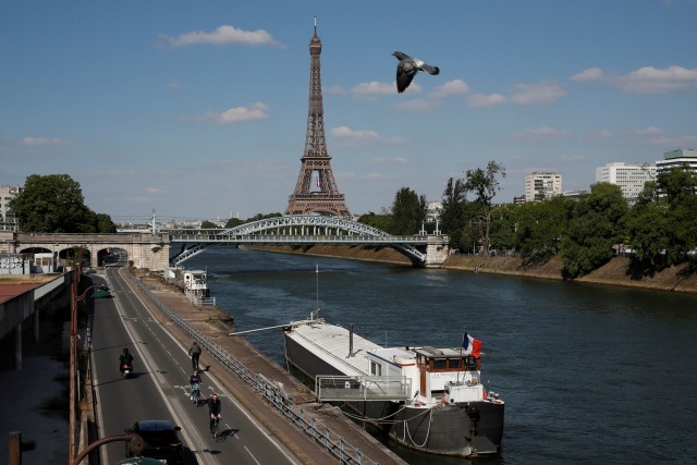 Orang-orang mengendarai sepeda di jalur sepeda di tepi sungai Seine dengan jembatan Pont Rouelle dan menara Eiffel di Paris. Foto: EUTERS/Gonzalo Fuentes