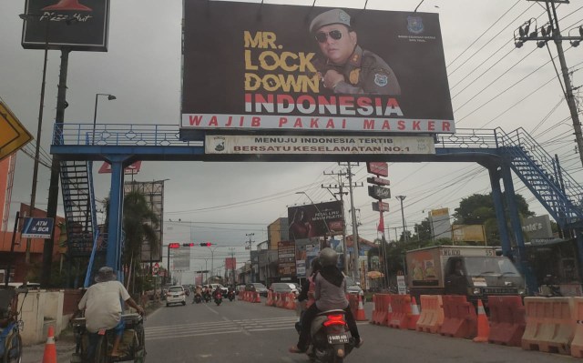 Warga tengah melintasi Jalan Mayjen Sutoyo dimana nampak billboard bergambar Wali Kota Tegal Dedy Yon Supriyono dan bertuliskan "Mr. Lockdown Indonesia. Wajib Pakai Masker", Senin (18/5/2020). (Foto: Setyadi)